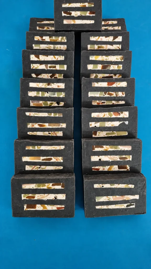 A studio arrangement of handcrafted charcoal soaps with colourful botanical inlays